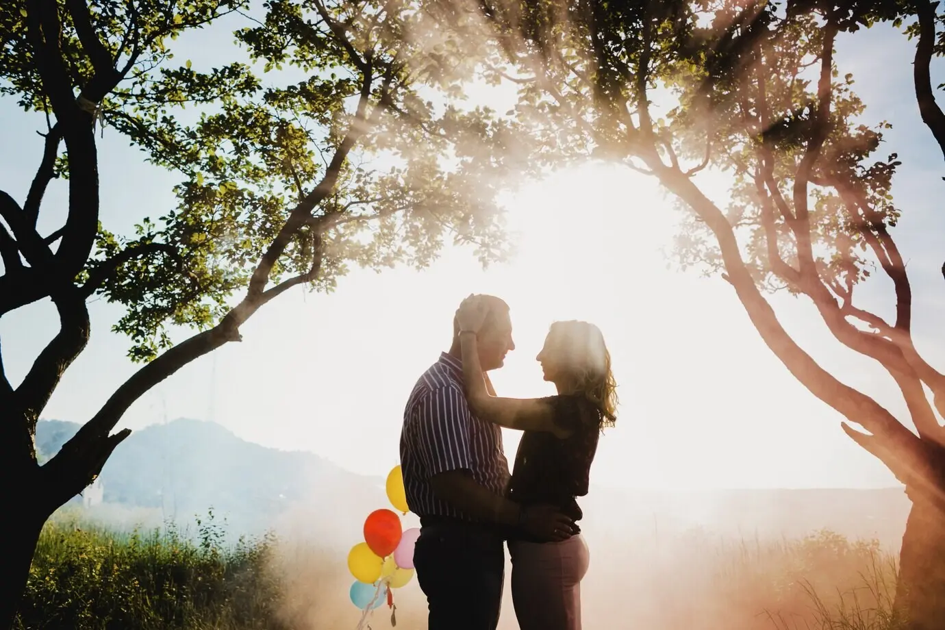 Очаровательная взрослая пара с разноцветными воздушными шарами стоит под деревом.